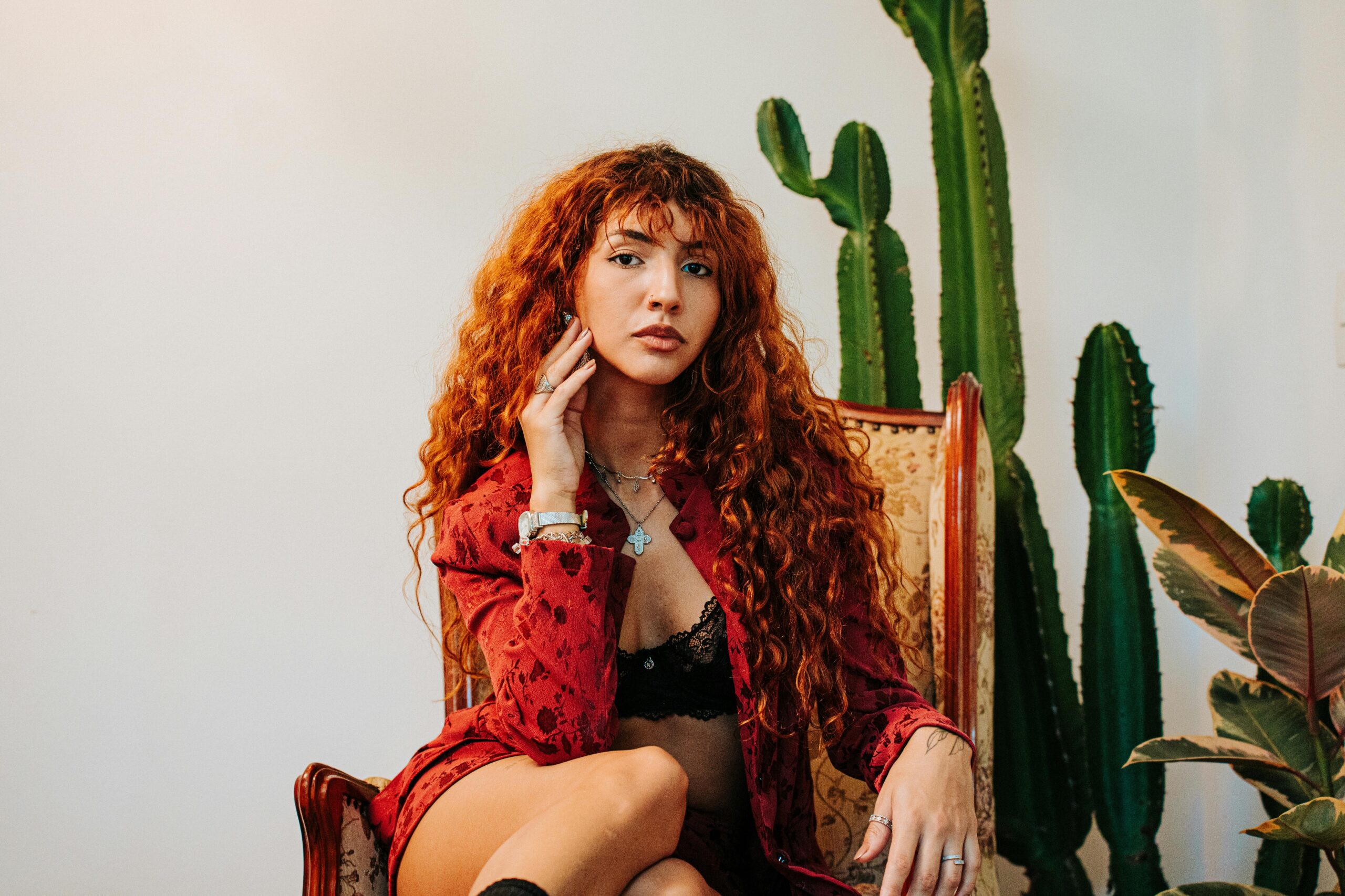 Fashionable woman with red hair poses in a chic setting with cacti in São Paulo.